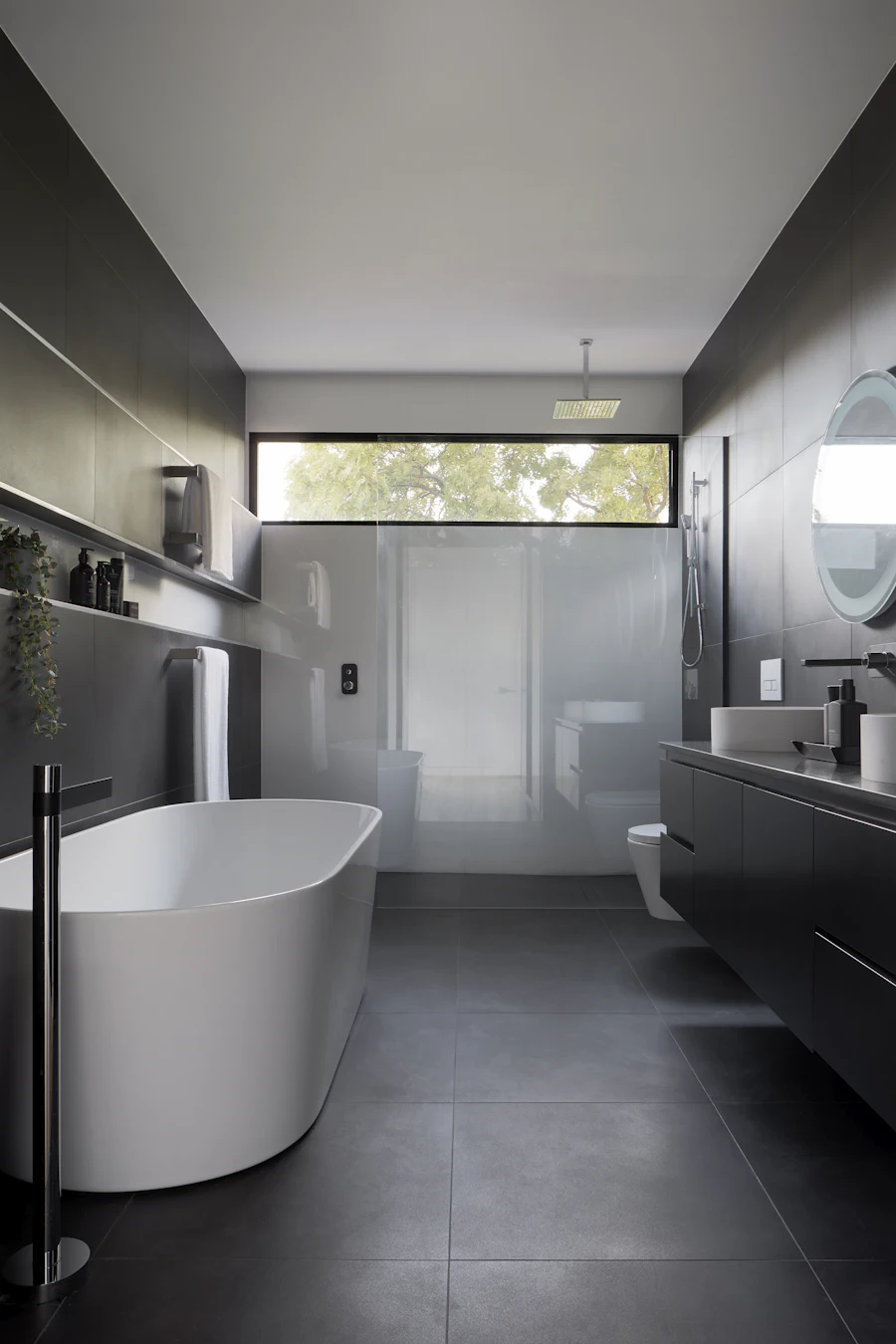 Dark-tiled bathroom with a freestanding bath and a glass-screened walk-in shower